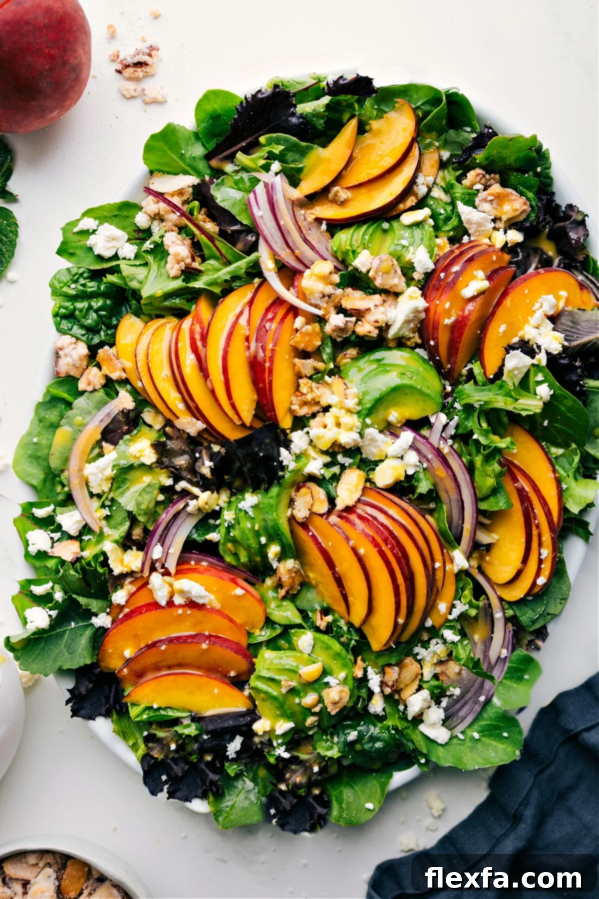 A refreshing peach salad featuring fresh peaches, thinly sliced red onions, crumbled feta cheese, and crunchy candied almonds, all served over a bed of crisp lettuce and lightly drizzled with a zesty dressing.