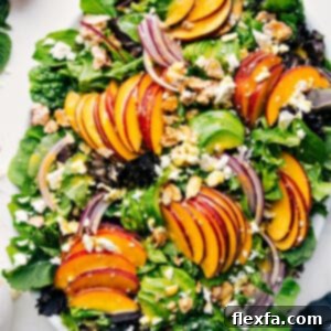 A vibrant peach salad featuring fresh peaches, red onions, feta, and candied almonds over a bed of mixed greens, drizzled with a delicious citrus dressing.