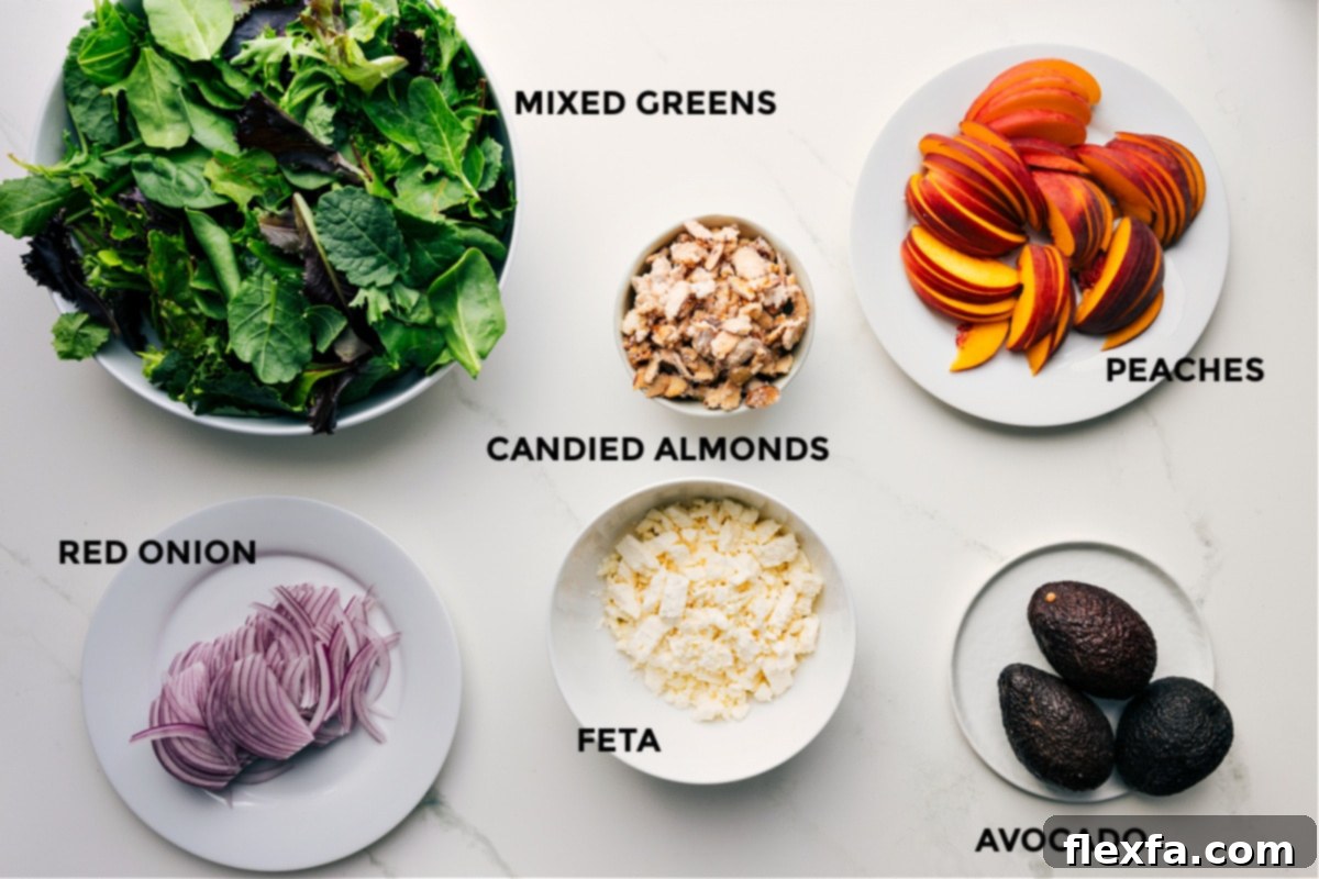 All the fresh ingredients for this peach salad, prepped and ready for assembly, including mixed greens, thinly sliced red onions, crumbled feta, candied almonds, diced avocado, and sliced peaches.
