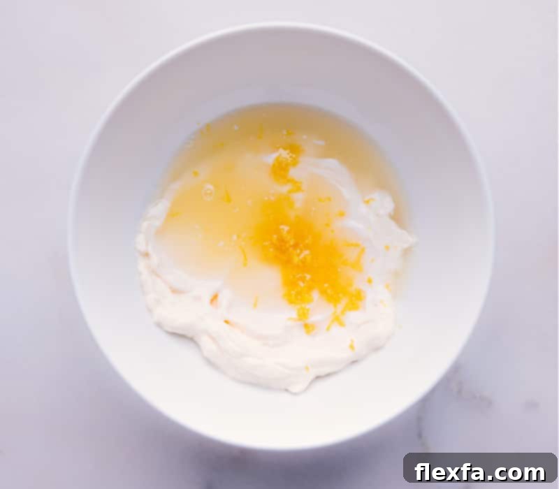 Follow these easy steps to combine simple ingredients into a tangy, zesty, and fresh Tartar Sauce recipe. Quick and effortless for gourmet results. A process shot showing ingredients like lemon juice, zest, dill, and relish being added to a bowl of mayonnaise, illustrating the initial steps of making Tartar Sauce.