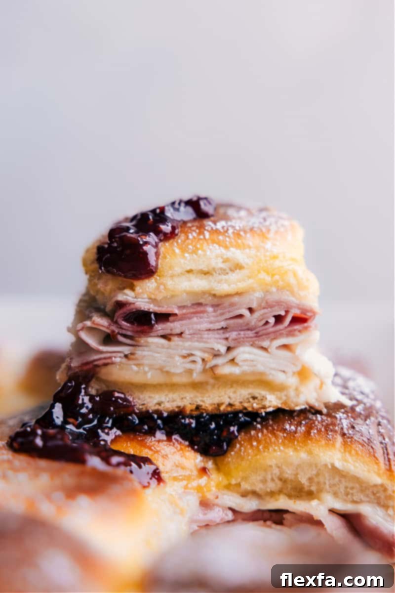 Stacked Monte Cristo Sliders, golden brown and dusted with powdered sugar, ready to be served with berry jam.