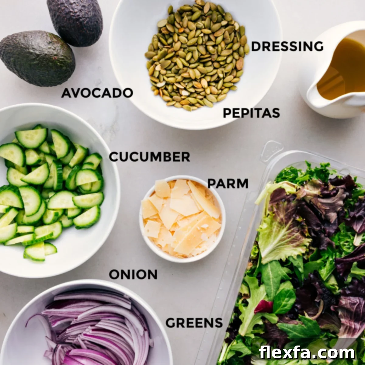 All the vibrant, fresh ingredients for this Everyday Salad Recipe are meticulously prepped and arranged, including a rich dressing, crunchy pepitas, creamy avocado, crisp cucumber, finely shaved Parmesan, mixed greens, and thinly sliced red onion, ready for effortless assembly.
