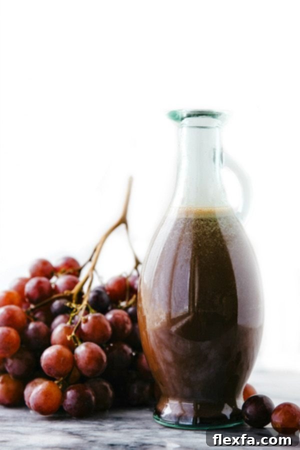 Homemade cherry balsamic salad dressing in a clear container, accompanied by fresh red grapes, perfect for a delicious and refreshing fruit salad.