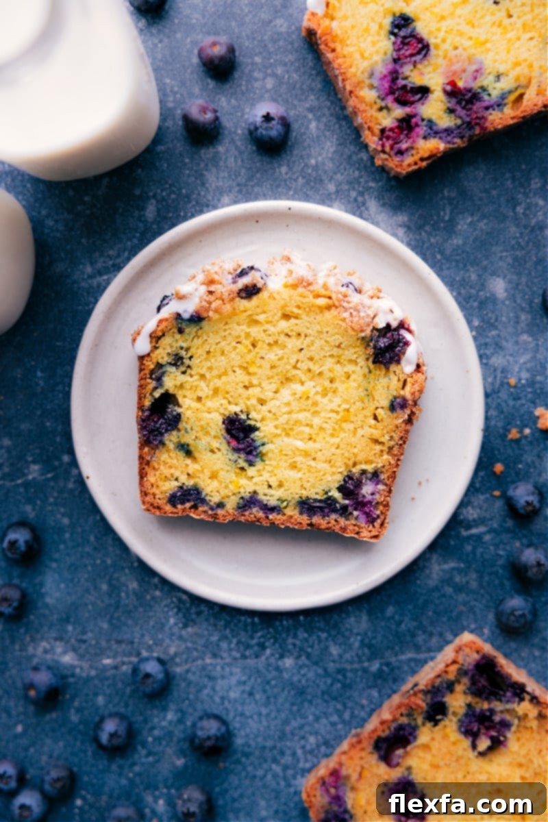 Lemon Blueberry Bread Slice - Moist and Irresistible A perfectly sliced piece of lemon blueberry bread, showcasing its moist, tender interior filled with blueberries and topped with a delicate lemon glaze.