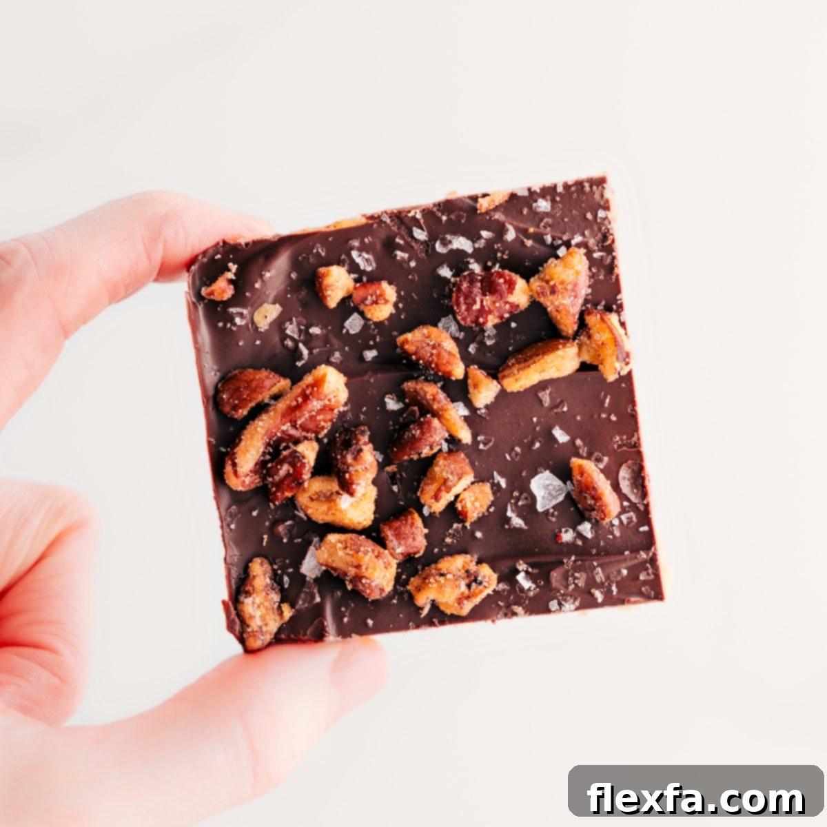 A Christmas Crack square is held up, topped with candied pecans.