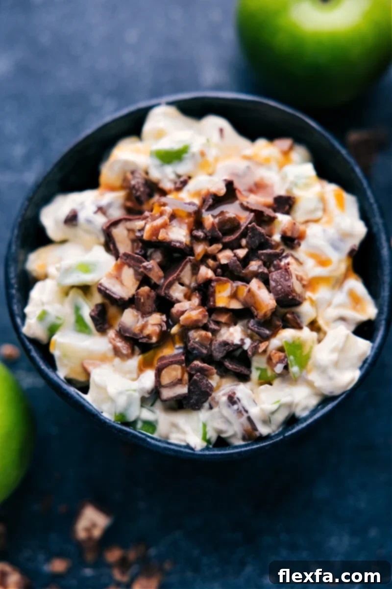 An inviting up-close overhead shot of a finished Snickers Salad in a serving bowl, garnished with extra diced Snickers pieces, a sprinkle of toffee bits, and a luscious caramel drizzle.