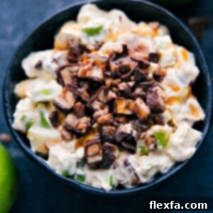 A serving of Snickers Salad, showcasing the creamy pudding base, chunks of Snickers, and diced green apples in a glass bowl.