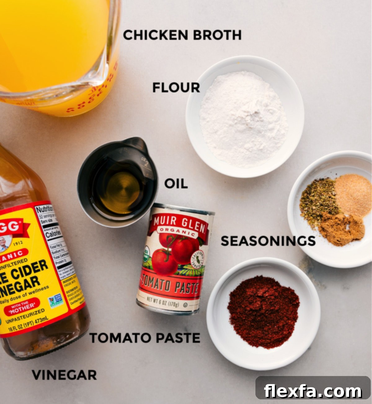 All the fresh ingredients for this homemade enchilada sauce recipe are prepped and neatly arranged on a counter, including chicken broth, flour, various seasonings, oil, tomato paste, and a bottle of apple cider vinegar, ready for easy assembly and cooking.