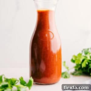 A bowl of rich red enchilada sauce, garnished with a sprig of fresh cilantro, sitting beside a wooden spoon, indicating its deliciousness and readiness for cooking.