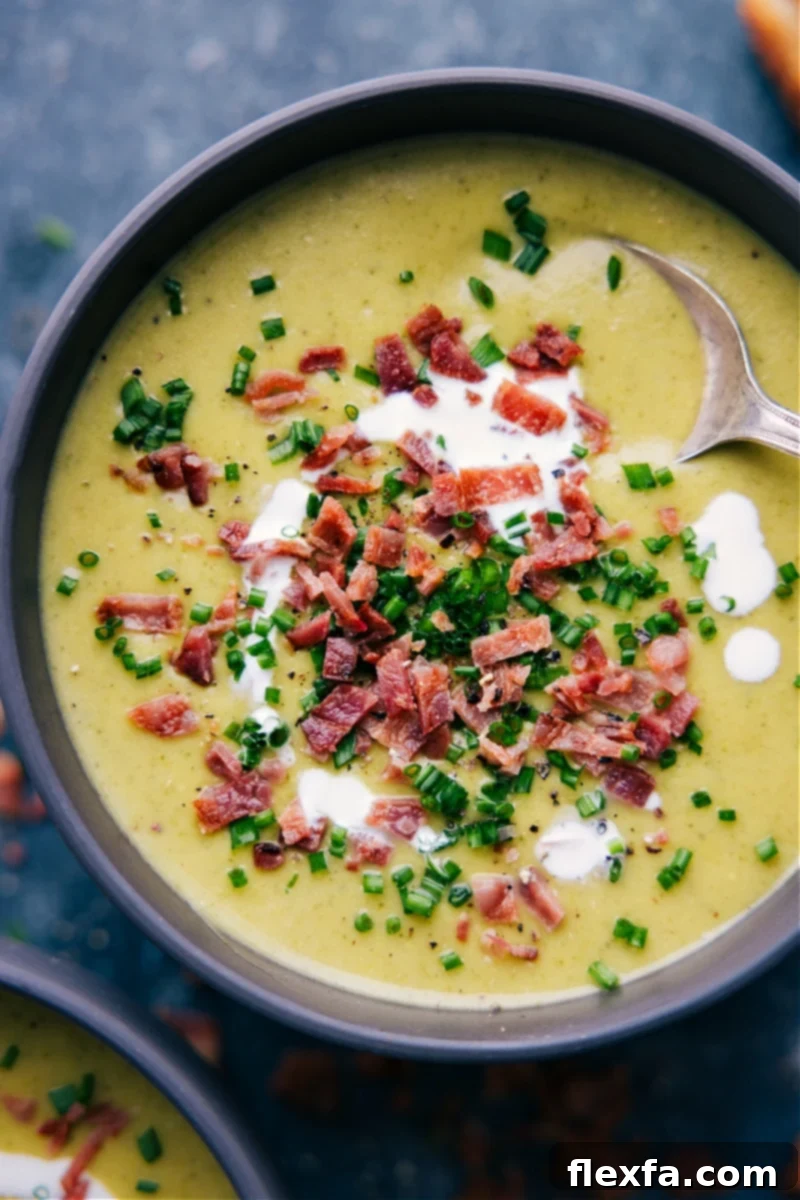 A top-down view of a steaming bowl of creamy and cheesy broccoli soup, garnished with a swirl of cream and fresh parsley.