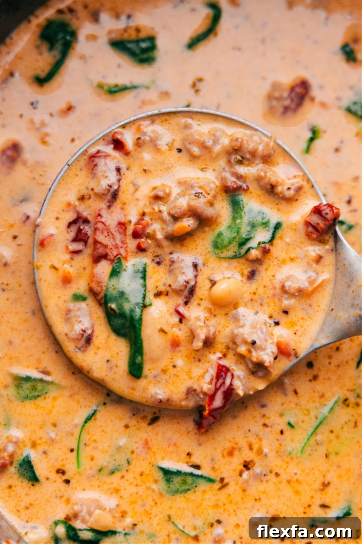 A ladle scooping a generous portion of the best creamy Tuscan soup from a large pot, showing the rich texture and all the delicious ingredients.