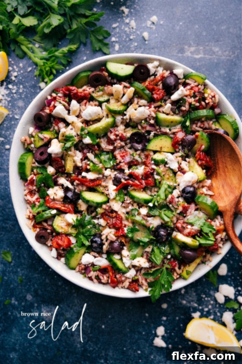 Craft a delicious, healthy Mediterranean-inspired Brown Rice Salad! This recipe combines nutty brown rice with crisp cucumbers, roasted red peppers, sun-dried tomatoes, red onion, parsley, and crumbled feta cheese, all in a zesty lemon dressing. Perfect for a quick, easy, family-friendly side dish or light meal. Overhead shot of a vibrant Mediterranean Brown Rice Salad, garnished with fresh parsley and a lemon wedge, showcasing its colorful ingredients and inviting texture.