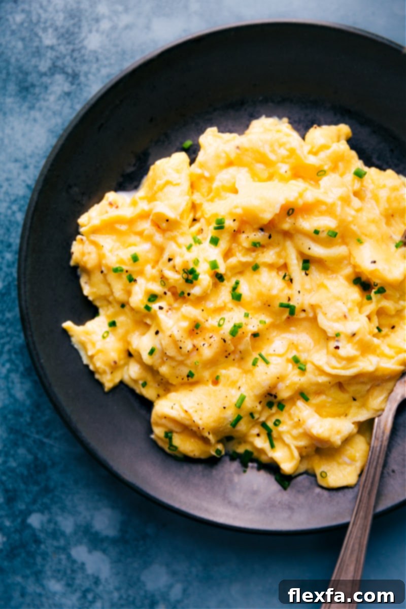 Close-up overhead view of a serving of fluffy, creamy scrambled eggs on a plate, garnished with fresh chives, indicating a perfect breakfast.