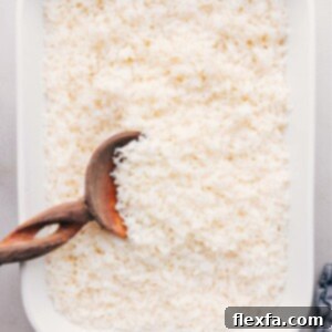 How To Make White Rice fresh out of the oven. A close-up of perfectly cooked, fluffy white rice in a baking dish, garnished with a sprig of fresh herb.