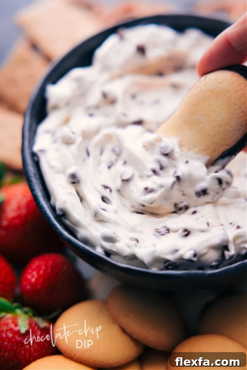 Creamy Chocolate Chip Dip served in a white bowl, with a Milano cookie gently dipped into the indulgent mixture, ready to be enjoyed. The dip is speckled with mini chocolate chips.