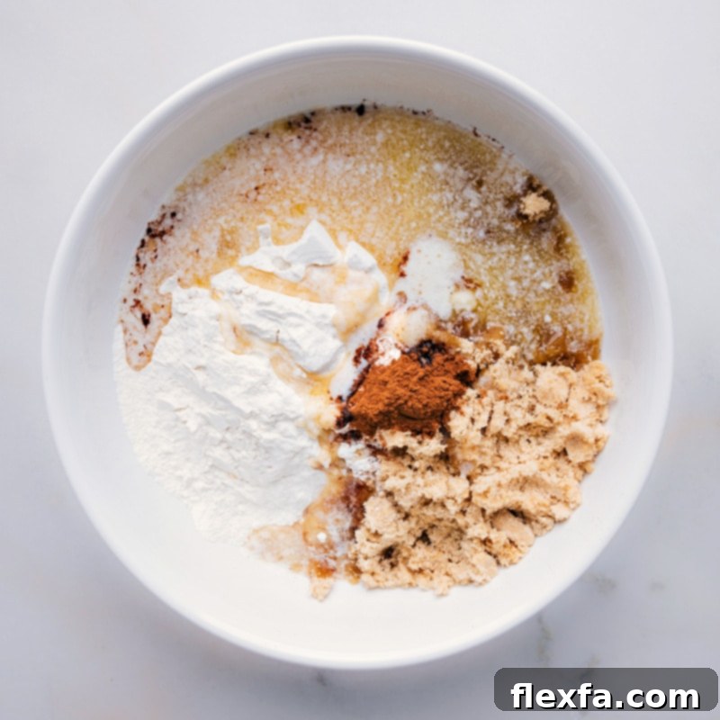 Process shot showing cooled melted butter being poured into a bowl with dry streusel ingredients (flour, brown sugar, cinnamon, salt).