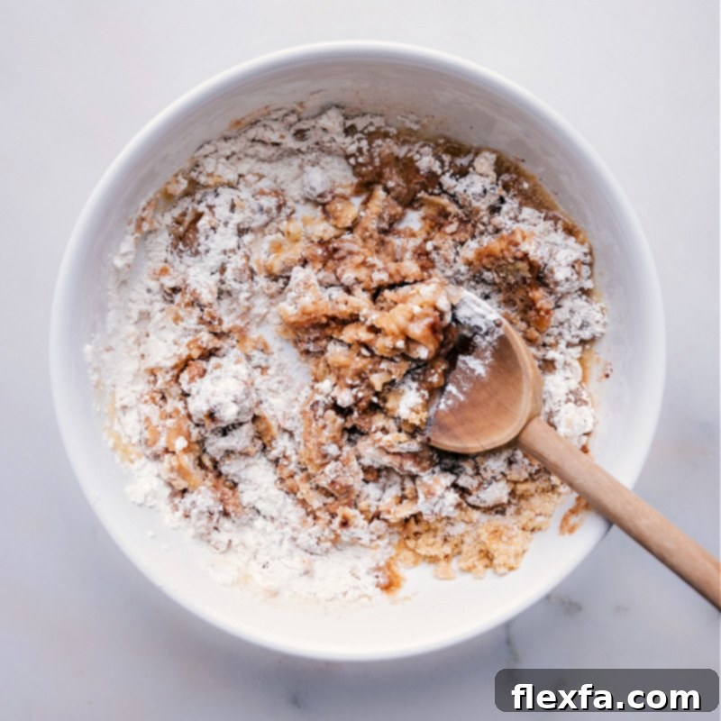 Process shot of streusel ingredients being mixed together in a bowl, forming coarse crumbs.