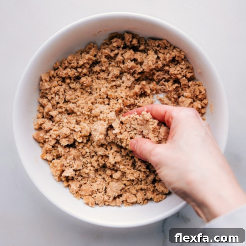 Process shot of a hand gently mixing streusel ingredients together in a bowl, creating the desired crumbly texture.
