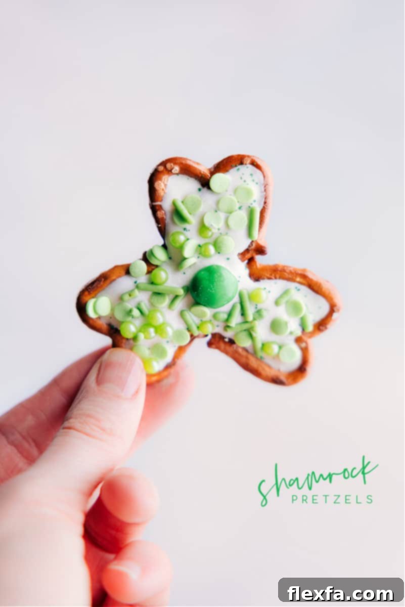 A hand holding up a finished Pretzel Shamrock, showcasing its festive green and white design.
