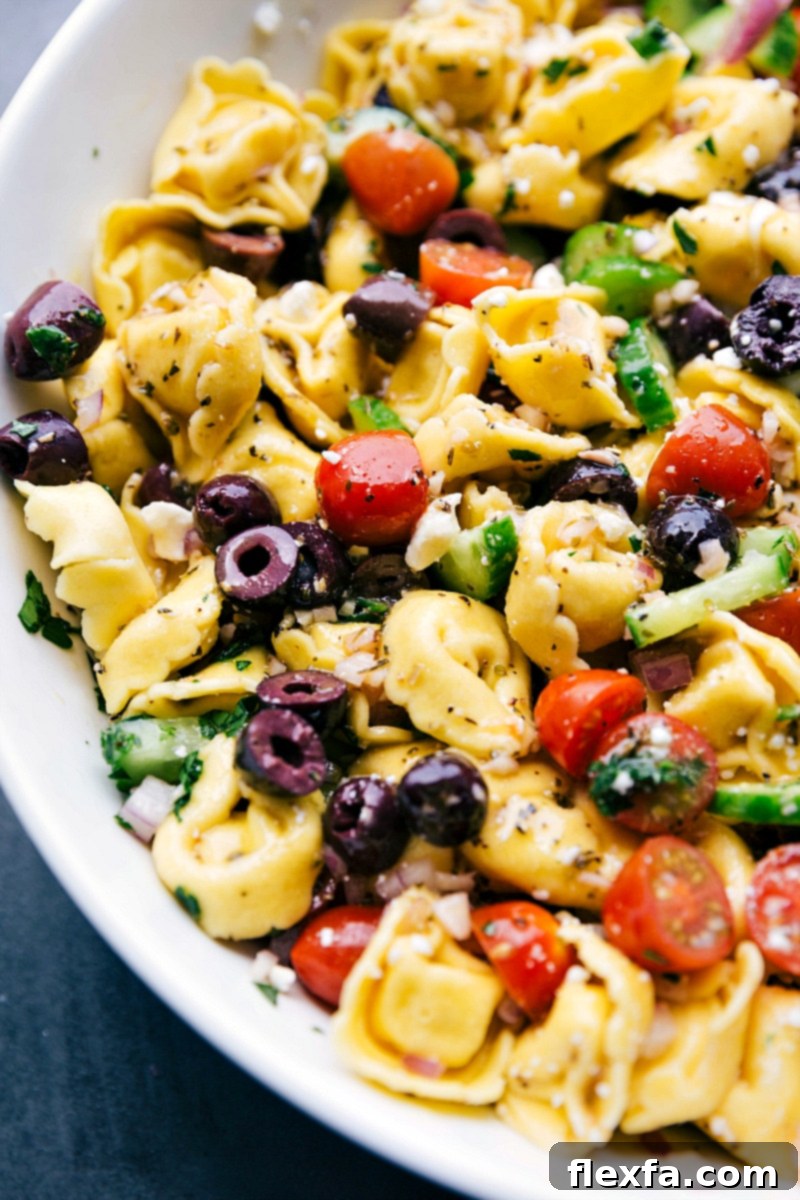 A large bowl of finished Greek tortellini salad, perfectly tossed and ready to be served, showcasing its colorful ingredients and appetizing texture.