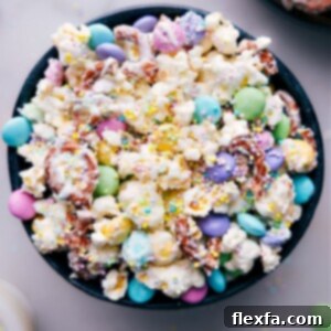 A close-up image of Easter Popcorn on a white platter, showcasing the texture and vibrant colors of the chocolate, pretzels, and M&M's.