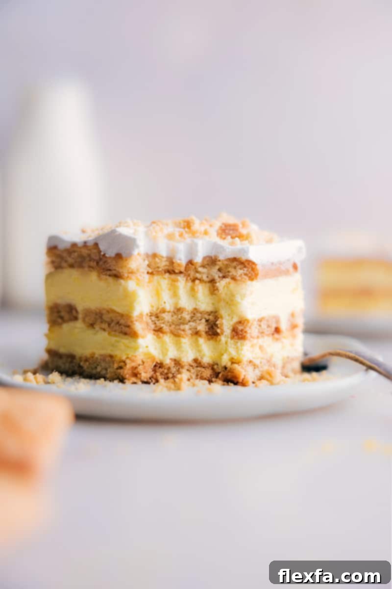 A close-up view of a perfectly sliced piece of Lemon Icebox Cake with a small bite taken out, clearly showing the alternating layers of creamy lemon filling and soft, buttery shortbread cookies, garnished with lemon zest.