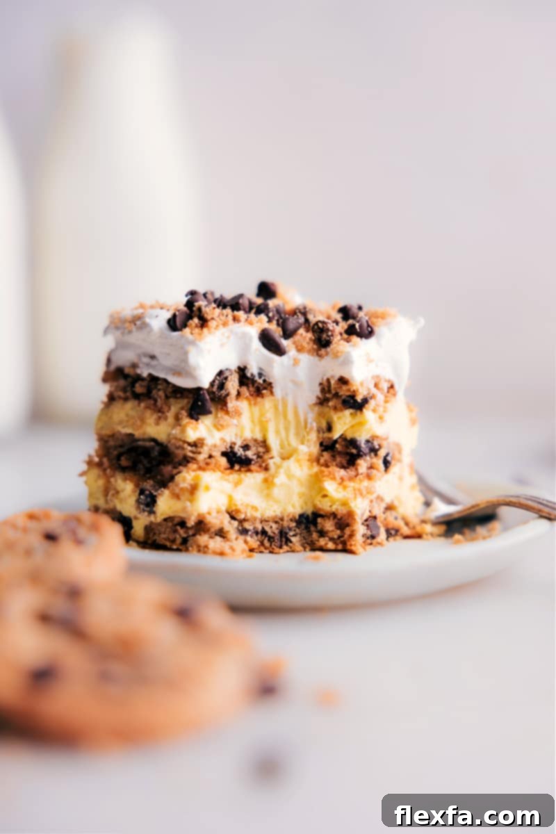 A close-up image of a luscious slice of Chocolate Chip Cookie Icebox Cake on a white plate, with a fork having taken a bite. The distinct layers of softened chocolate chip cookies and creamy vanilla filling are clearly visible, showcasing the cake's inviting texture.