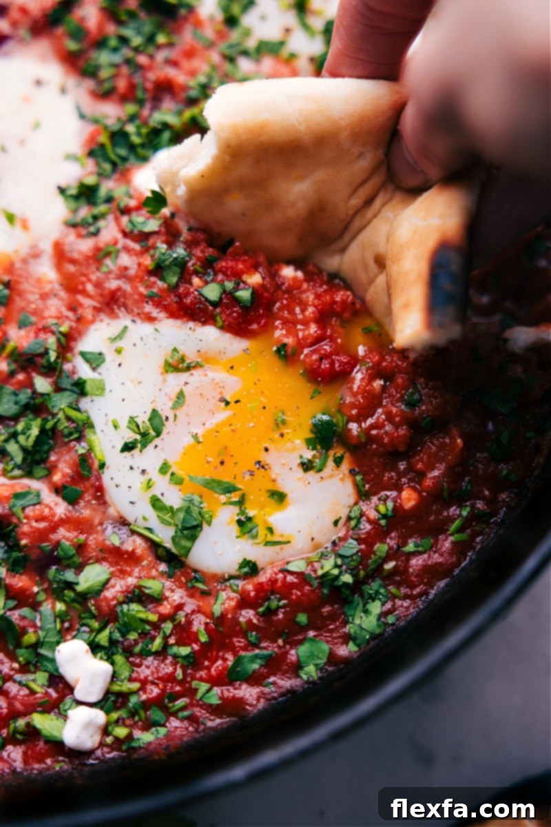 Overhead view of a sizzling Shakshuka dish in a pan, with perfectly poached eggs in a vibrant red tomato sauce, garnished with fresh herbs, ready to be served with warm bread.