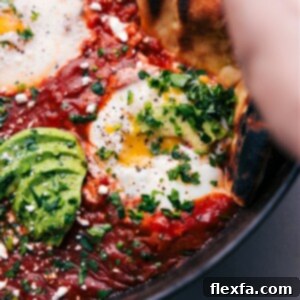 A vibrant Shakshuka dish in a cast iron pan, featuring perfectly poached eggs in a rich, spiced tomato sauce, garnished with fresh herbs.
