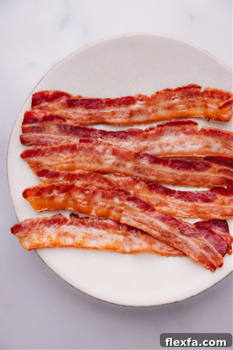 Overhead image of a complete breakfast plate with crispy baked bacon, scrambled eggs, and toast, ready to be enjoyed