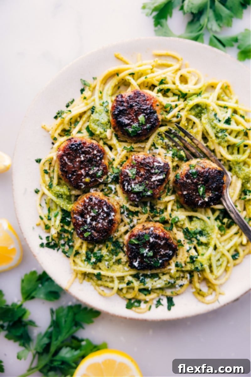 Overhead image of delicious oven-baked chicken meatballs on a bed of vibrant pesto pasta, garnished with fresh basil leaves.