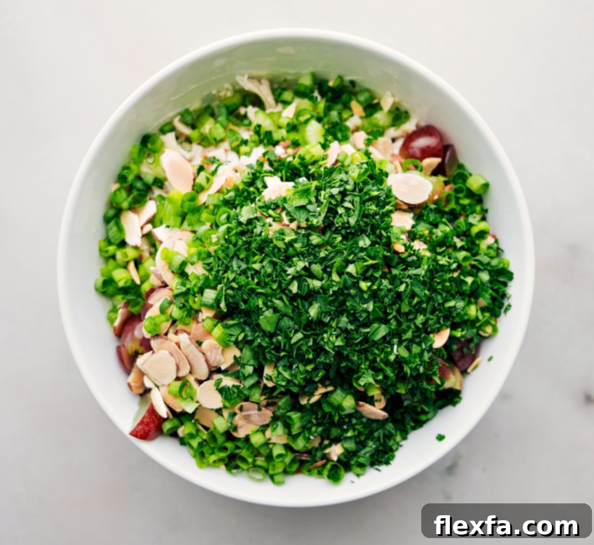 All the prepped ingredients for healthy chicken salad being added to a large bowl, ready to be tossed together with the creamy dressing.