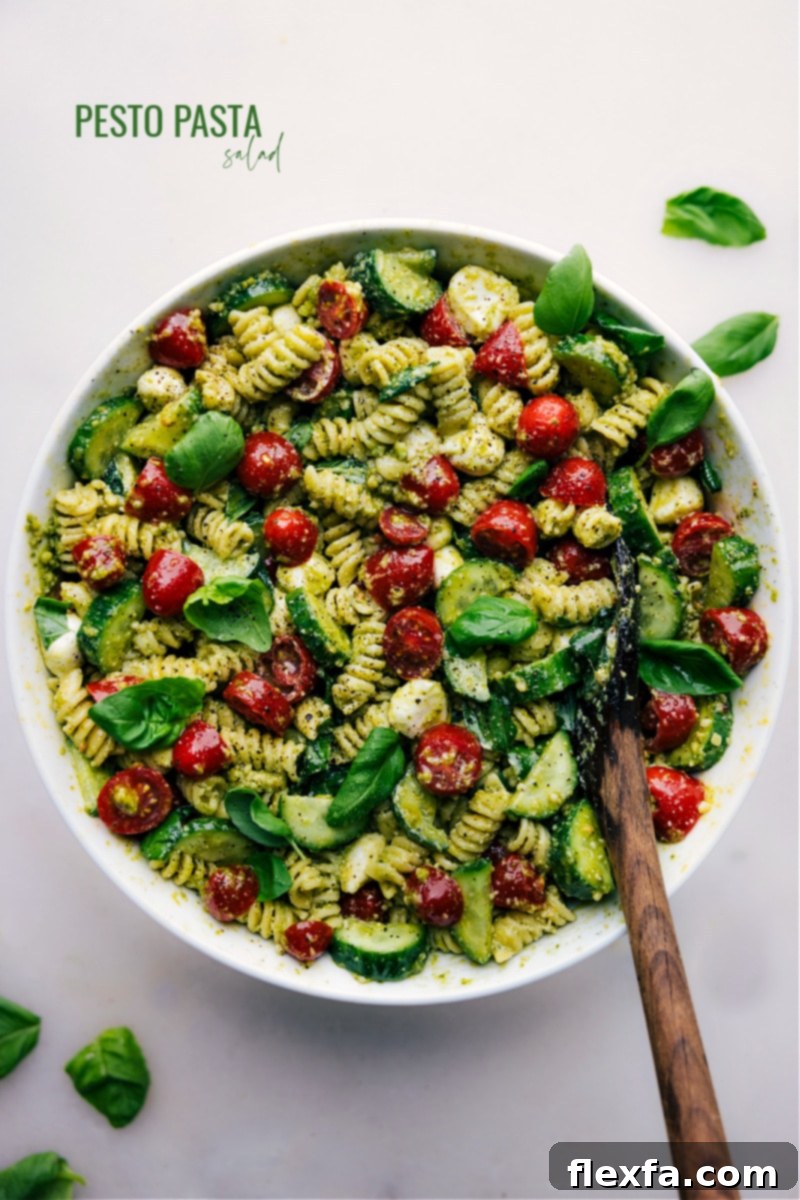 Fresh Pesto Pasta Delight 2 Overhead image of the vibrant Pesto Pasta Salad with perfectly cooked rotini pasta, halved cherry tomatoes, sliced cucumbers, and creamy mozzarella pearls, all generously coated in a rich green pesto sauce, garnished with fresh basil leaves.