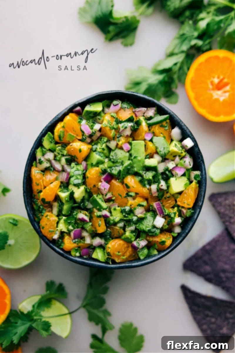 Avocado-Orange Salsa served in a white bowl with a spoon, surrounded by tortilla chips.