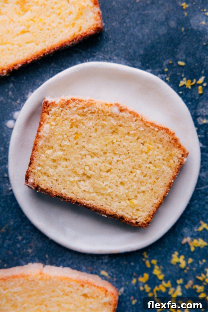 A beautifully sliced piece of Iced Lemon Bread on a white plate, showcasing its moist texture and vibrant lemon glaze.