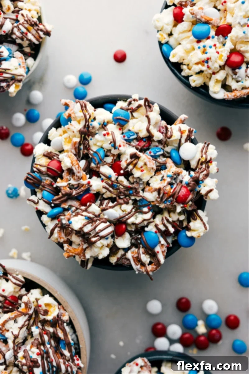 A large, inviting bowl of 4th of July Popcorn, richly decorated with red, white, and blue candy, festive sprinkles, and pretzel pieces, set against a blurred background, signaling a celebratory atmosphere.