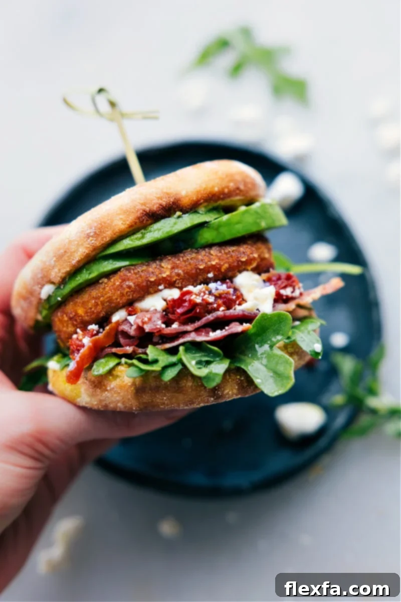 A hand holding up a perfectly assembled English muffin sandwich, showcasing the generous and delicious layers of ingredients inside.