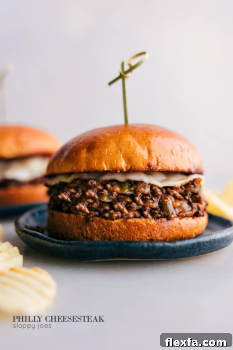 A close-up of a serving of Philly Cheesesteak Sloppy Joes on a plate, showcasing the saucy beef and melted provolone cheese on a toasted brioche bun.