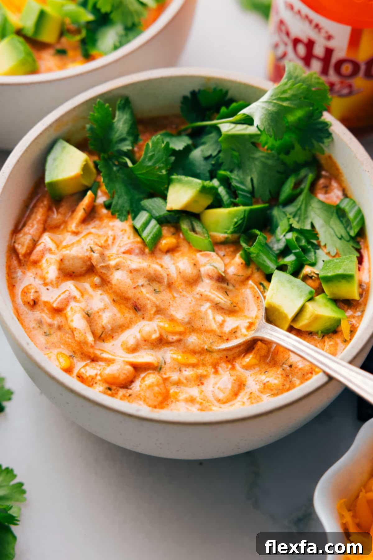 A big bowl of Buffalo Chicken Chili with a spoon in it. A perfect hearty meal for any occasion, garnished with fresh toppings.
