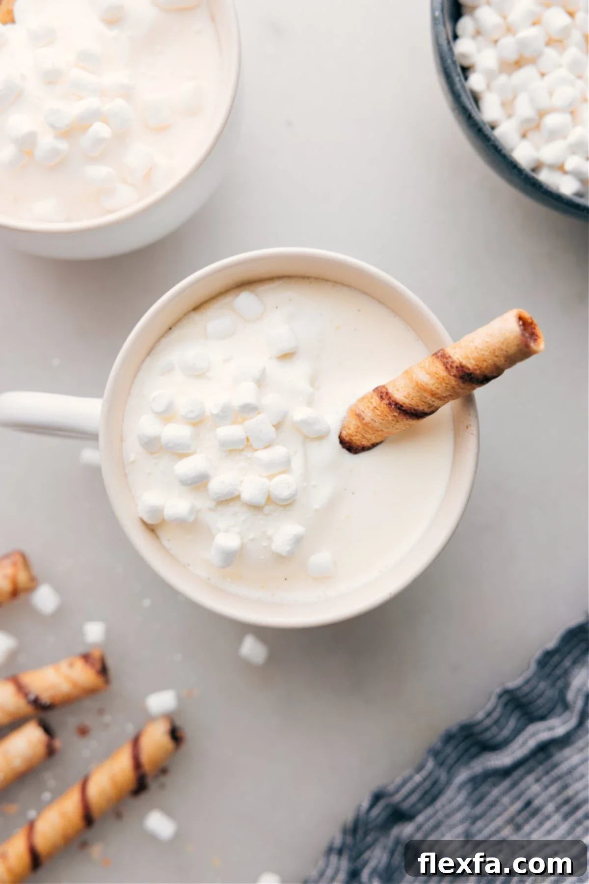 A mug of warm and delicious White Hot Chocolate, with marshmallows floating on top and a chocolate straw coming out of it.