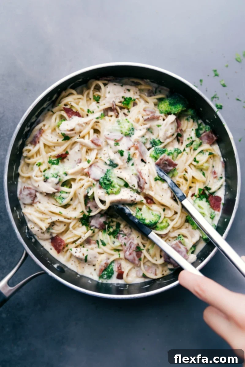 Chicken broccoli alfredo with tongs scooping up a creamy and delicious bite, ready to be enjoyed.