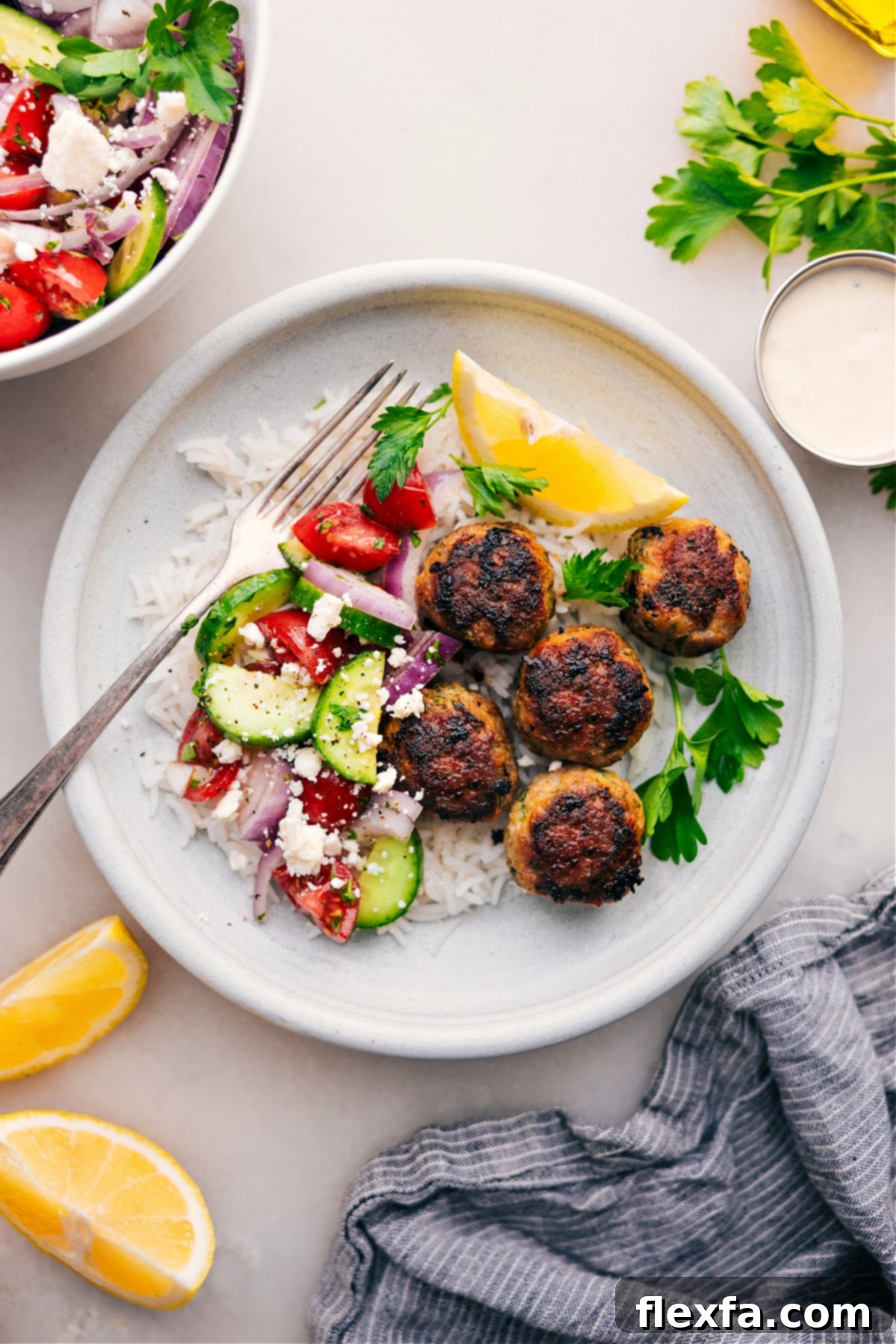 The Best Greek Turkey Meatballs Dinner Plate with Greek Turkey Meatballs served over a bed of fluffy rice with a fresh cucumber tomato salad on the side.