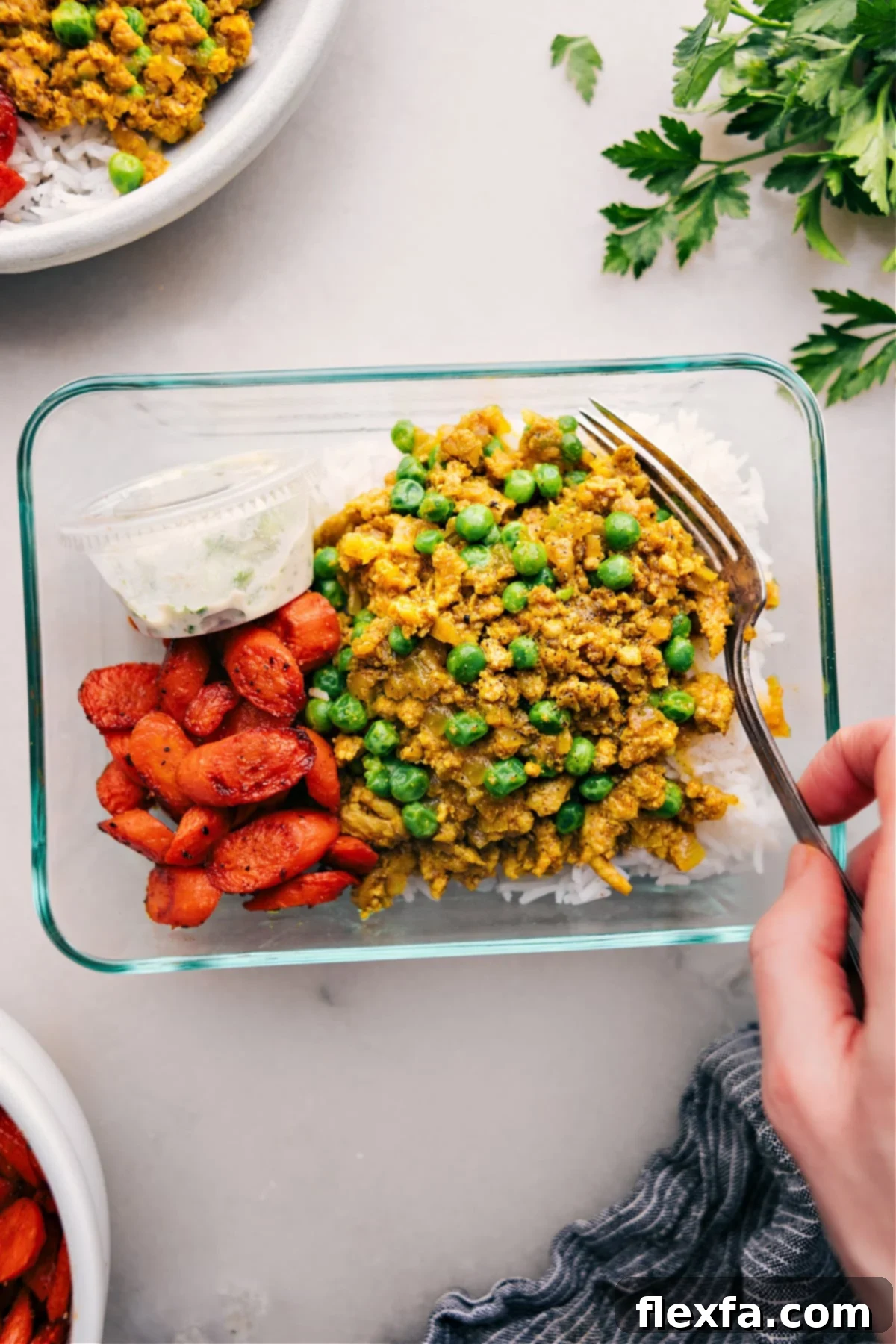 A beautifully meal-prepped glass container filled with fluffy basmati rice, savory Indian ground turkey, roasted vegetables, and a separate portion of cooling cucumber yogurt sauce, ready for a quick and satisfying meal.
