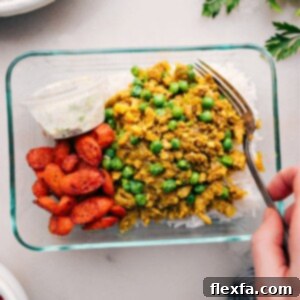 A meal-prepped glass container filled with basmati rice, savory Indian ground turkey, roasted vegetables, and a separate portion of cooling cucumber yogurt sauce, perfectly arranged for a quick and satisfying meal.