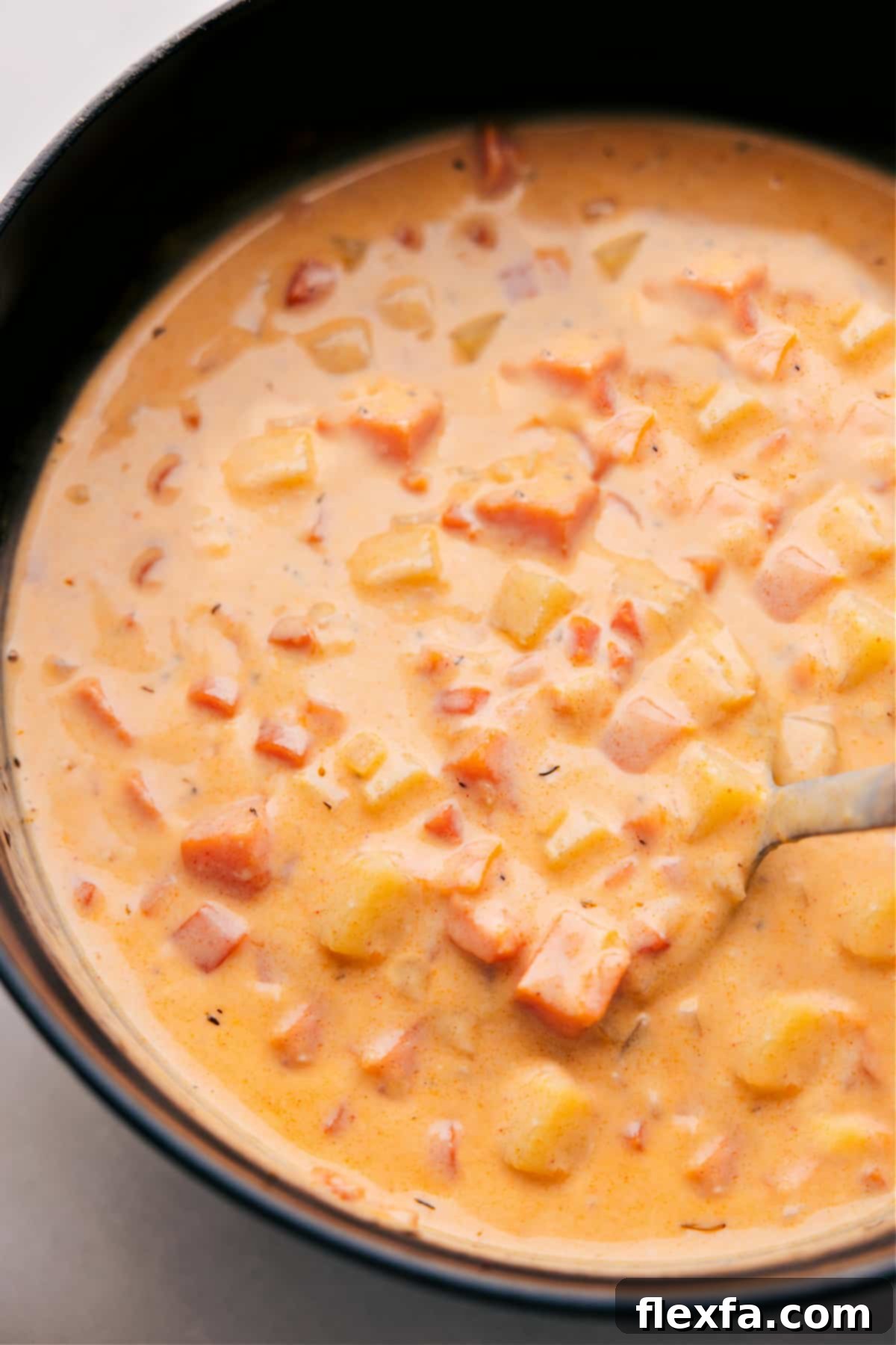 Overhead photo of a steaming bowl of Cheesy Potato Soup, garnished with crispy bacon and fresh herbs.