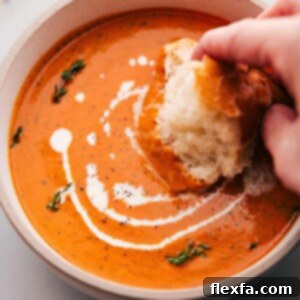 A large bowl of vibrant Roasted Red Pepper Soup, being served with crusty bread for dipping, showcasing its rich texture and inviting warmth.