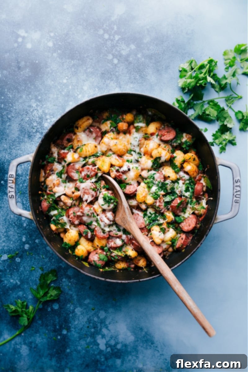 A vibrant close-up of White Bean Gnocchi in a skillet, showcasing tender gnocchi, white beans, sausage, tomatoes, and spinach topped with melted cheese, ready to serve.
