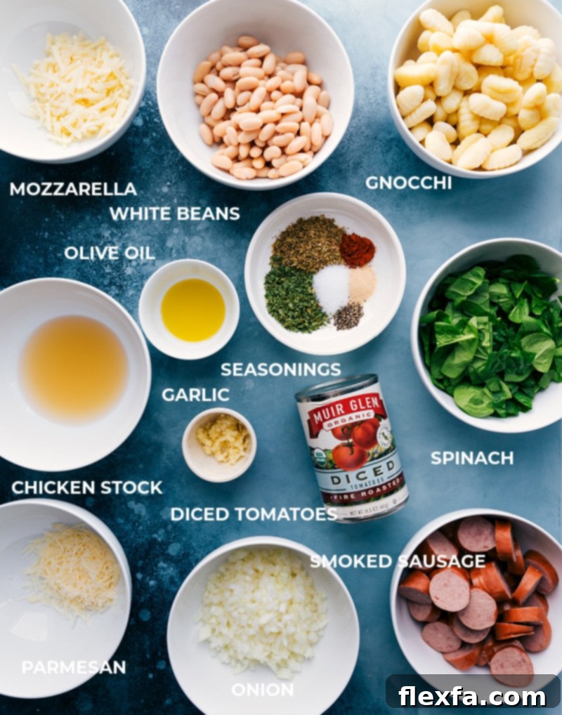 A flat lay of fresh ingredients for White Bean Gnocchi, including a package of gnocchi, canned white beans, fire-roasted tomatoes, smoked sausage, fresh spinach, onion, garlic, and various spices.