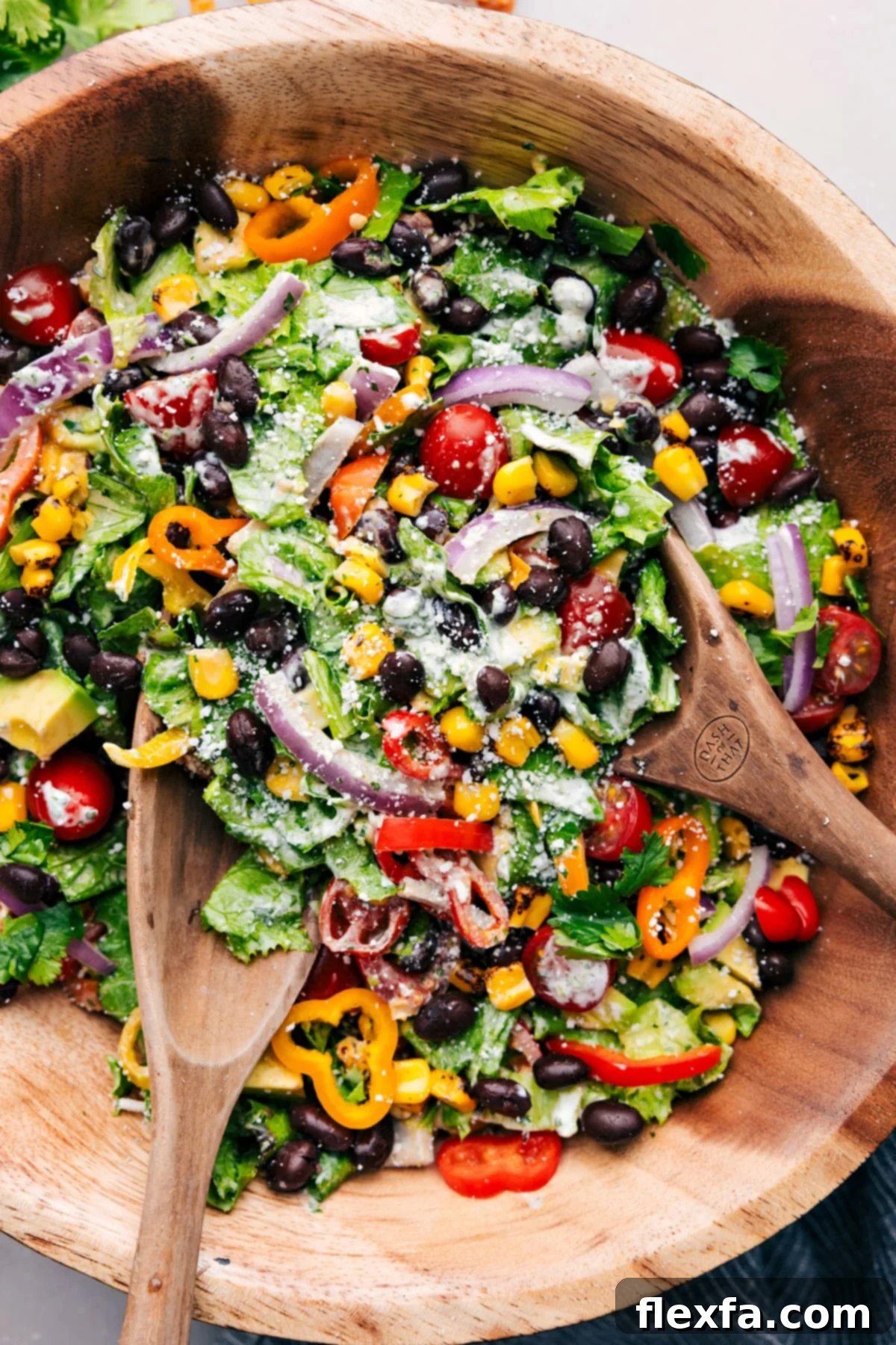The Best Mexican Salad with Cilantro-Lime Dressing A vibrant bowl of Mexican Salad tossed with serving utensils, showcasing black beans, corn, peppers, tomatoes, and a generous drizzle of cilantro-lime dressing.