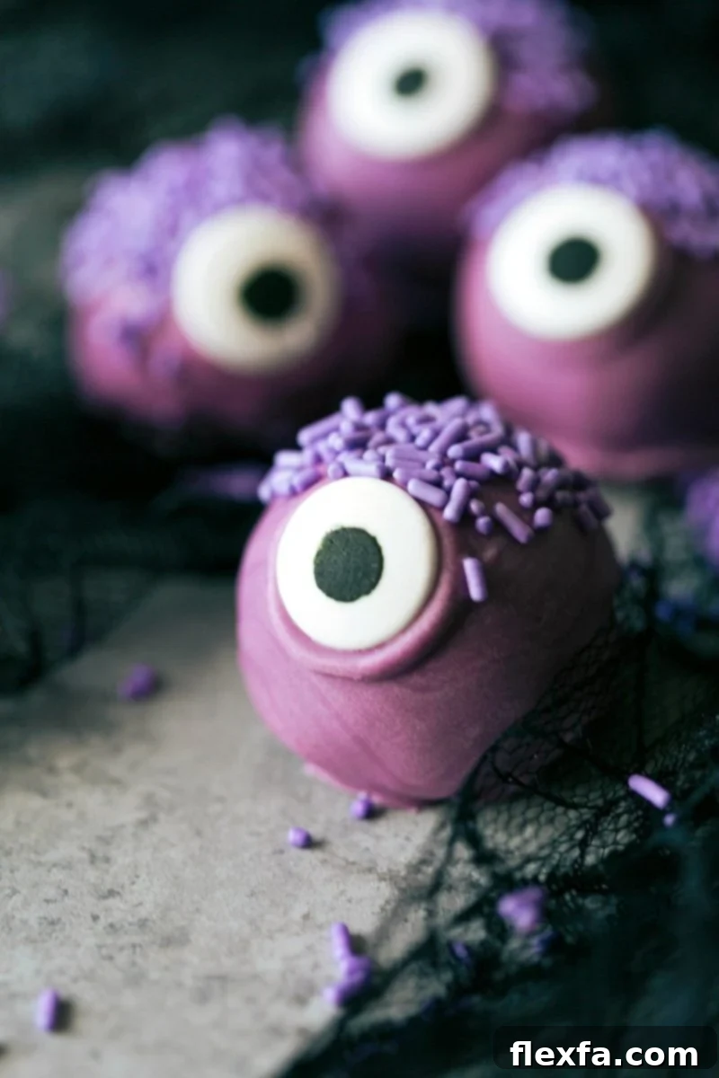 Four adorable and festive Halloween Oreo Truffles: a purple monster with one eye, an orange pumpkin with a pretzel stem, a brown bat with Oreo wings, and a white mummy with edible eyes.